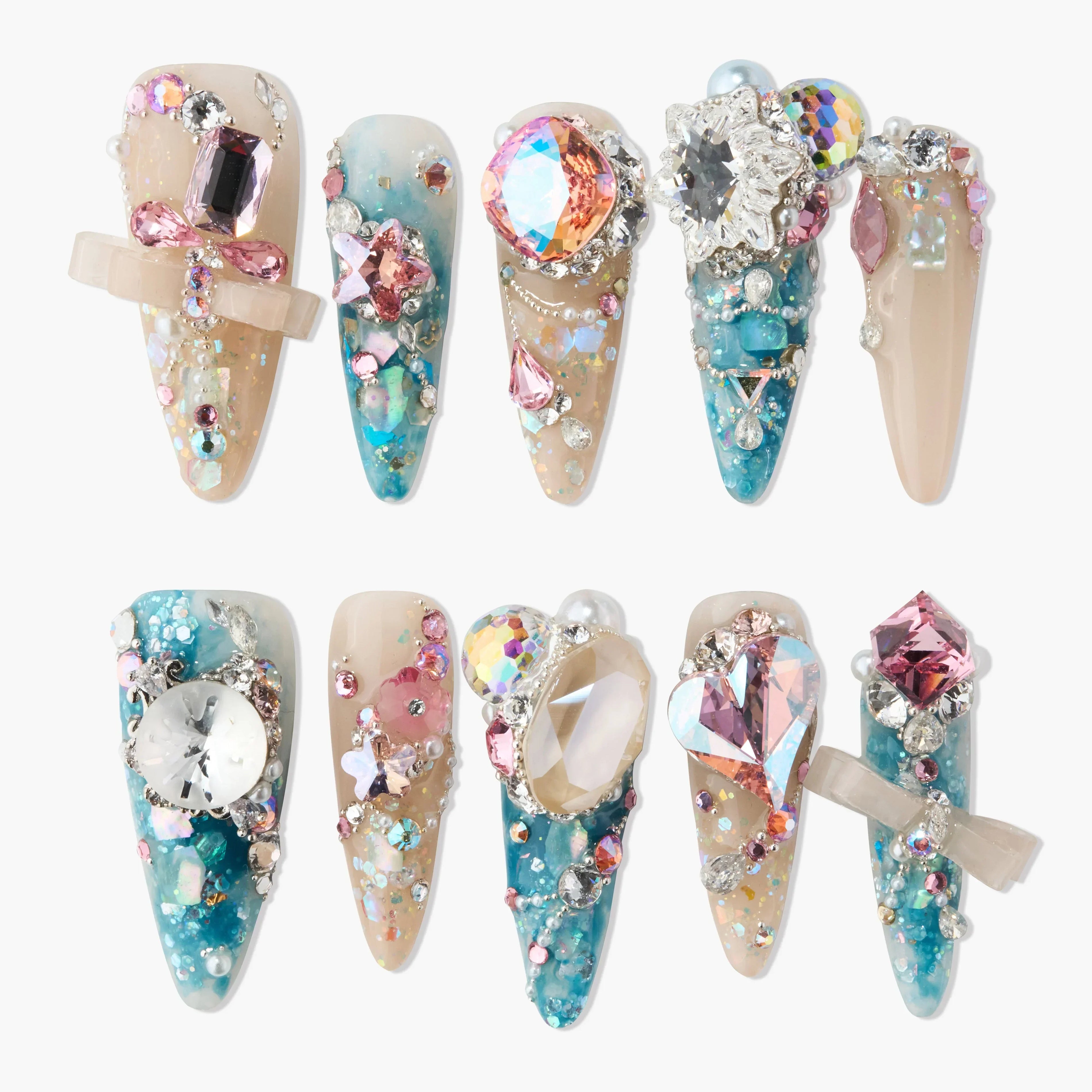 Handmade press-on nails with blue ombre, large colorful gems, and 3D bow accents