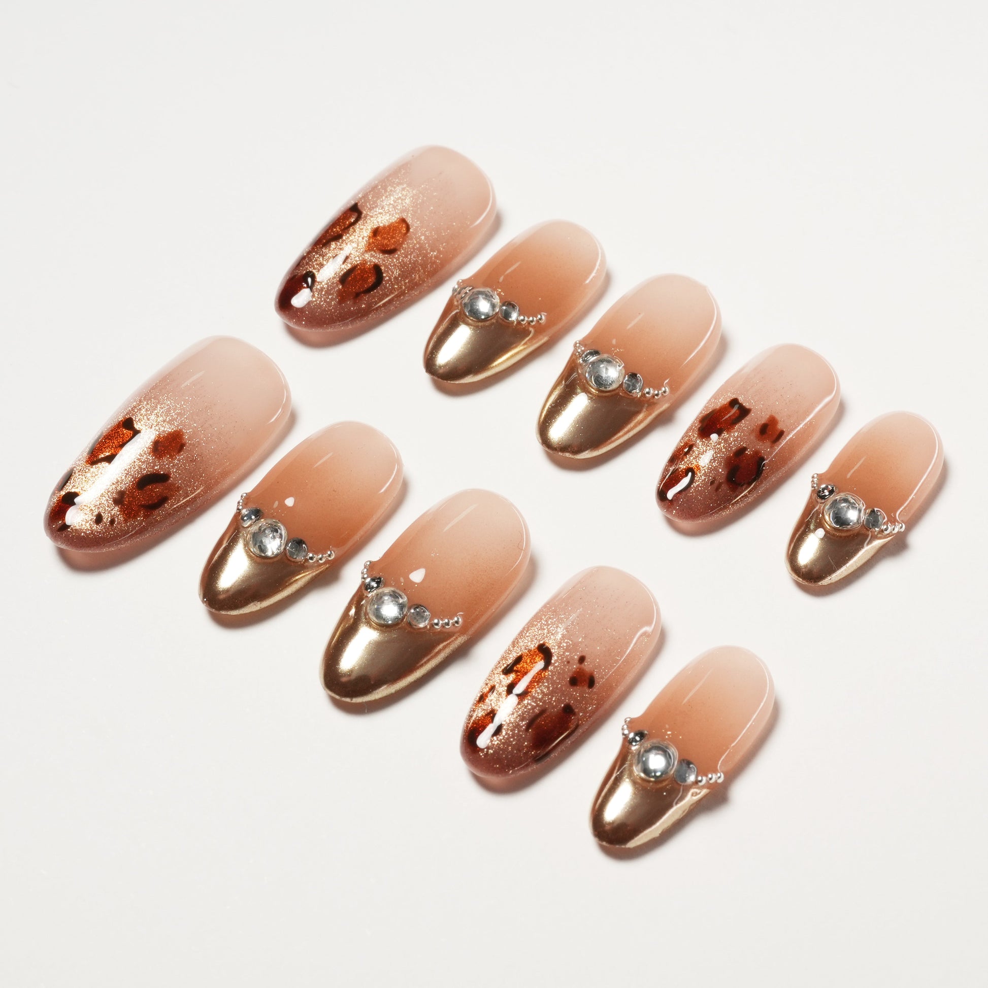 Handmade press-on nails with gold metallic tips, leopard print, and rhinestone accents.