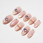 Pink and gold glitter press-on nails with rhinestone, bow, and heart gem accents