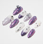 Handmade press-on nails in purple and white with star, bow, and gemstone accents