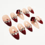 Handmade press-on nails with red tips, nude base, rhinestones, and large red gem accents.