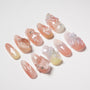 Handmade press-on nails with pink ombre, 3D bows, flowers, and rhinestone accents