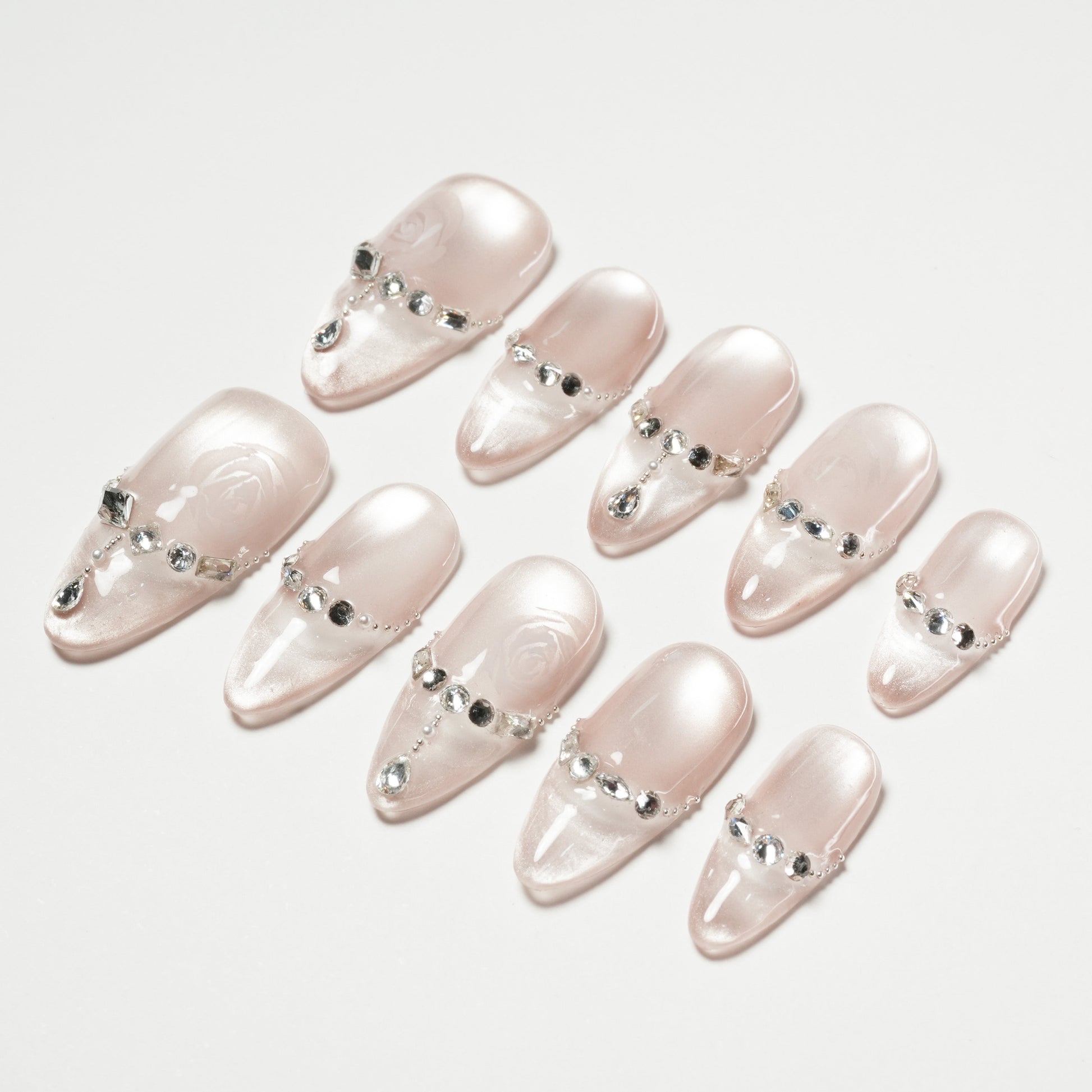 Glossy nude press-on nails with silver rhinestone accents arranged on a white background.