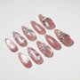 Handmade press-on nails with pink shimmer, glitter, butterfly accents, pearls, and rhinestones
