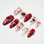 Red and white press-on nails with heart, bow, pearl, and gem designs on a white background