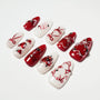 Red and white press-on nails with heart designs, pearls, and intricate nail art accents