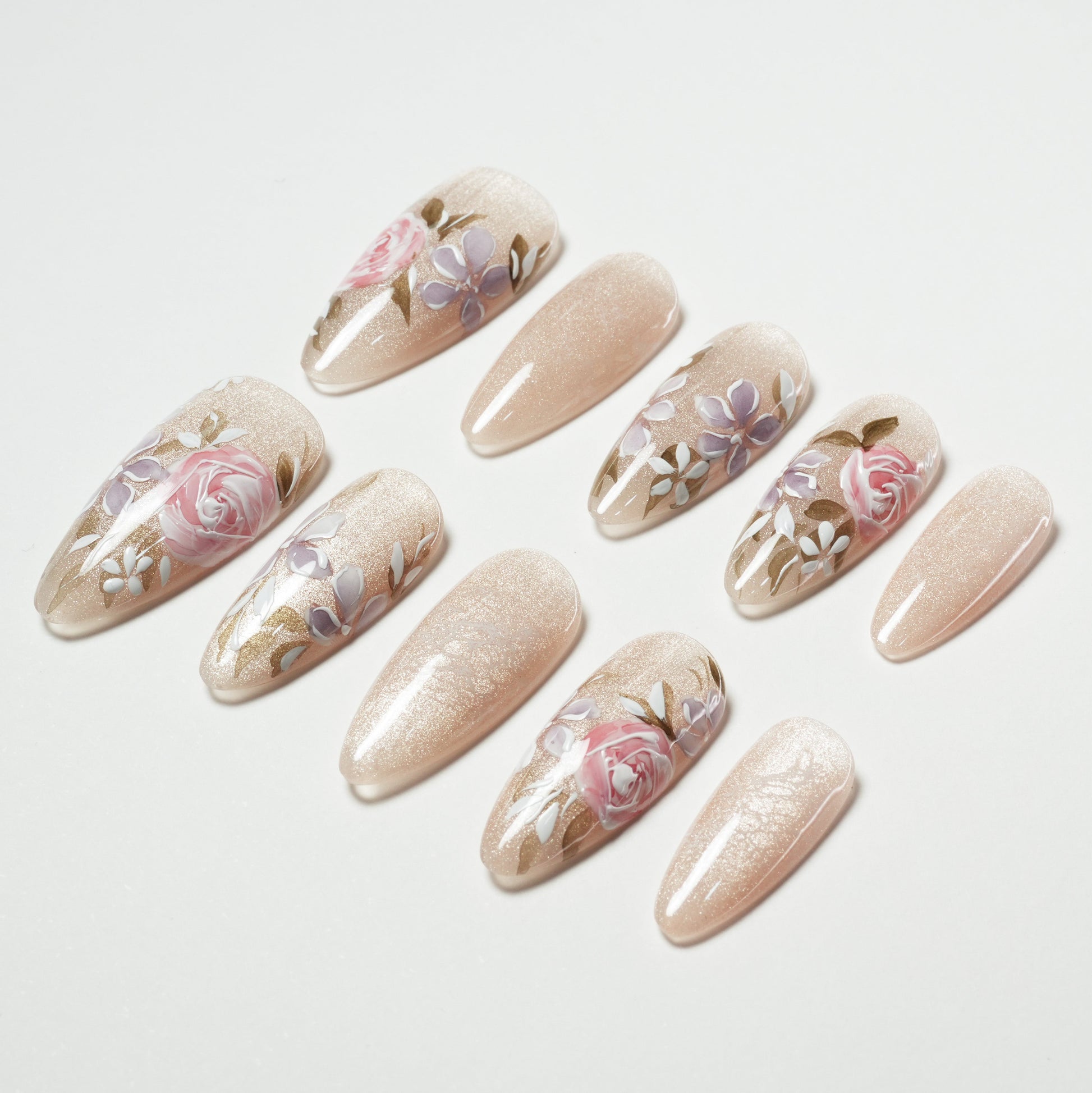 Handmade press-on nails with nude shimmer base and pink floral design, arranged on white background