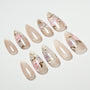 Handmade press-on nails with nude glitter base and pink floral designs, arranged on white background