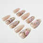 Handmade nude press-on nails with pink and purple floral design, arranged on white background