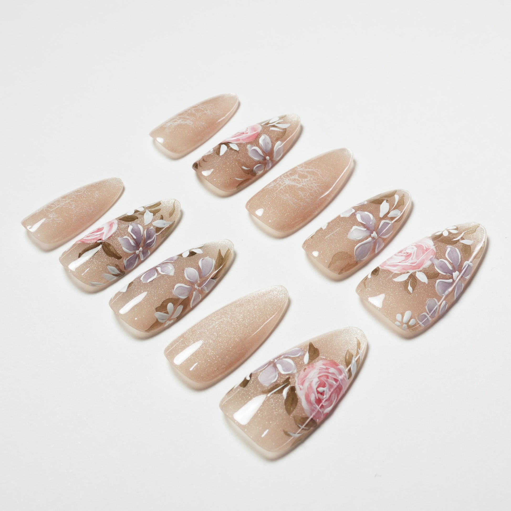 Handmade nude press-on nails with pink and purple floral design, arranged on white background