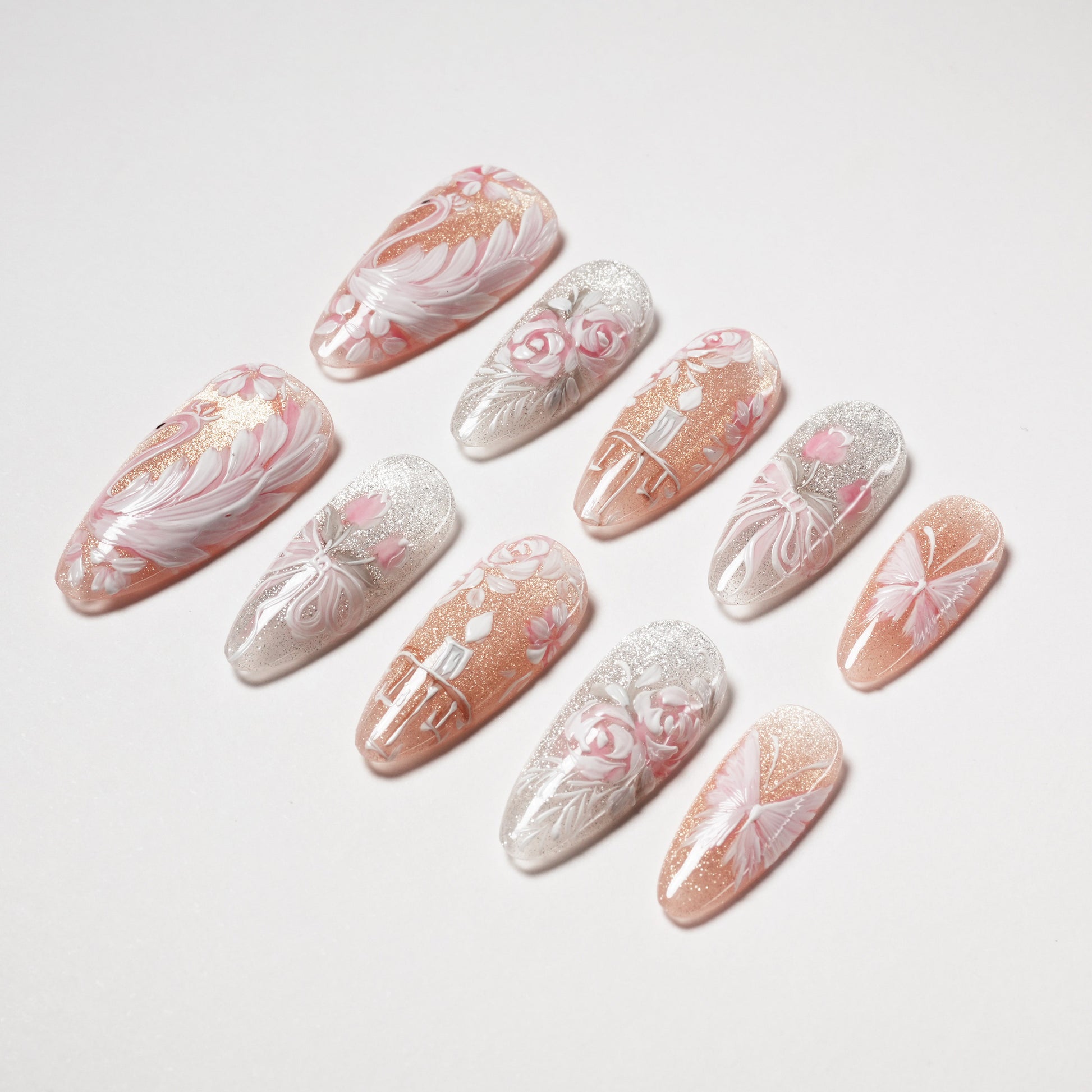 Handmade press-on nails with floral and feather designs in pink, white, and glitter accents