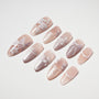 Handmade nude press-on nails with white floral designs and glitter accents