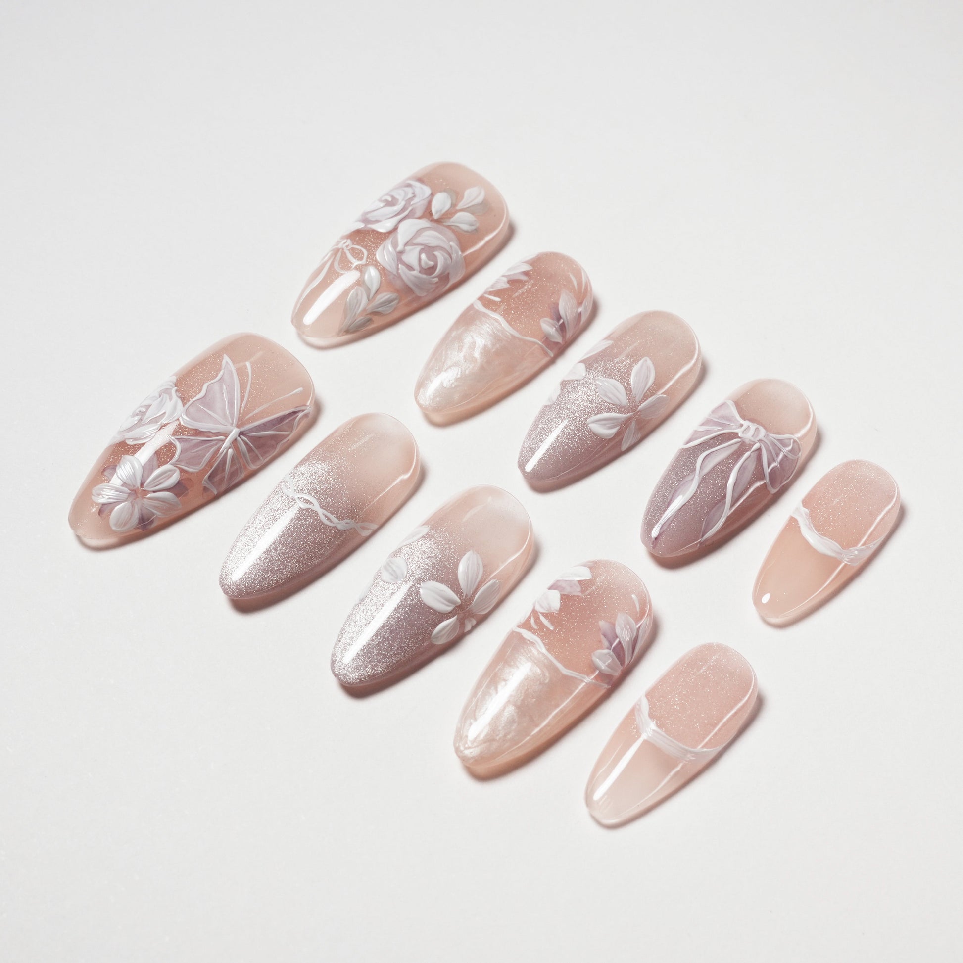 Handmade nude press-on nails with white floral designs and glitter accents