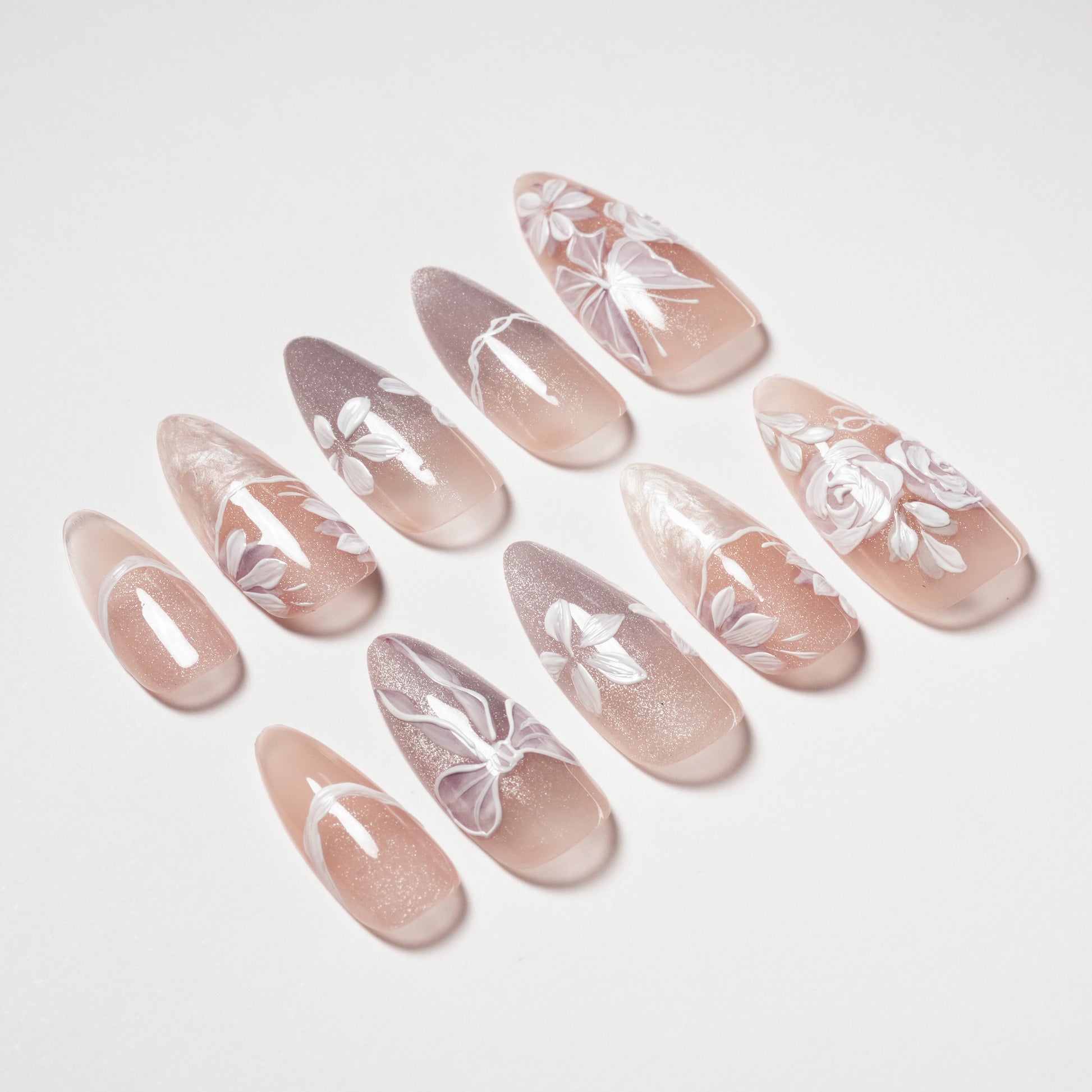 Handmade press-on nails with nude base and white floral designs, stiletto shape