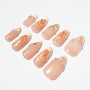 Handmade nude press-on nails with gold shimmer tips, floral art, and pearl rhinestone accents