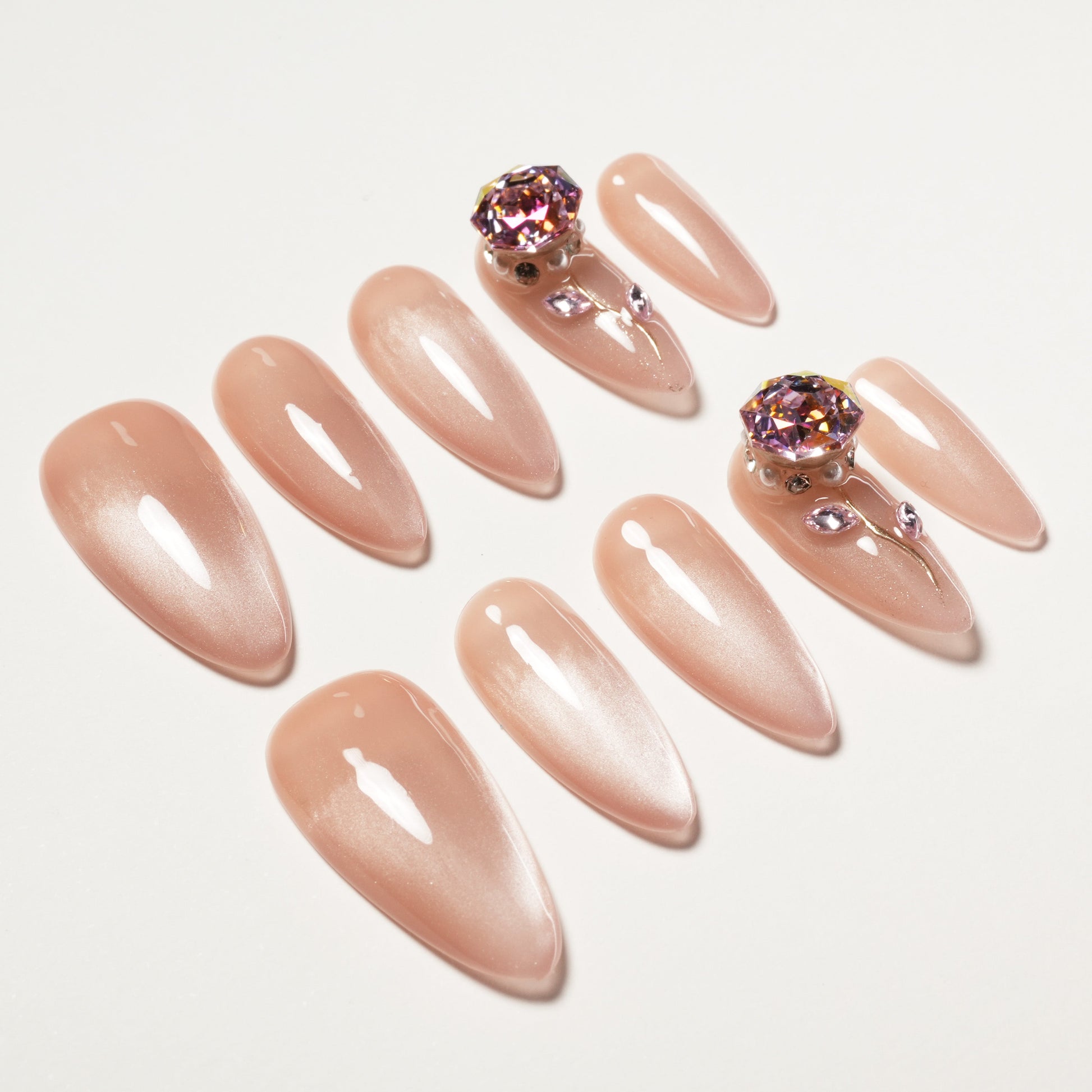 Glossy nude press-on nails set with gemstone and rhinestone accents on two nails