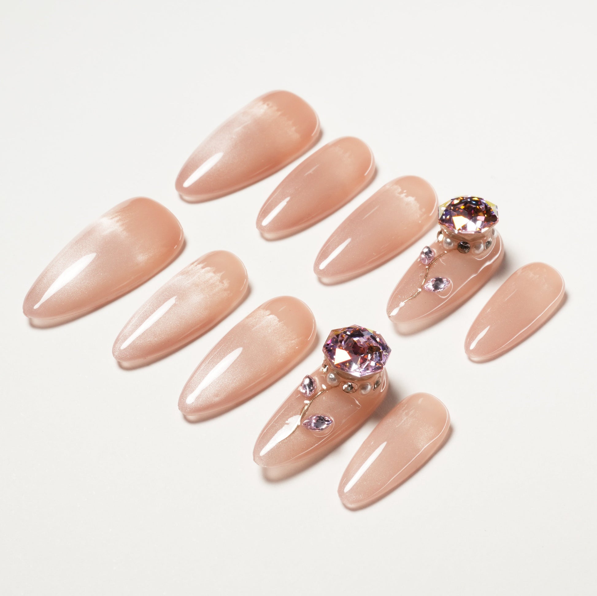 Glossy nude press-on nails with purple crystal and pearl accents on two nails, arranged on white background.