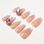 Nude almond press-on nails with pink gem and crystal 3D accents on white background