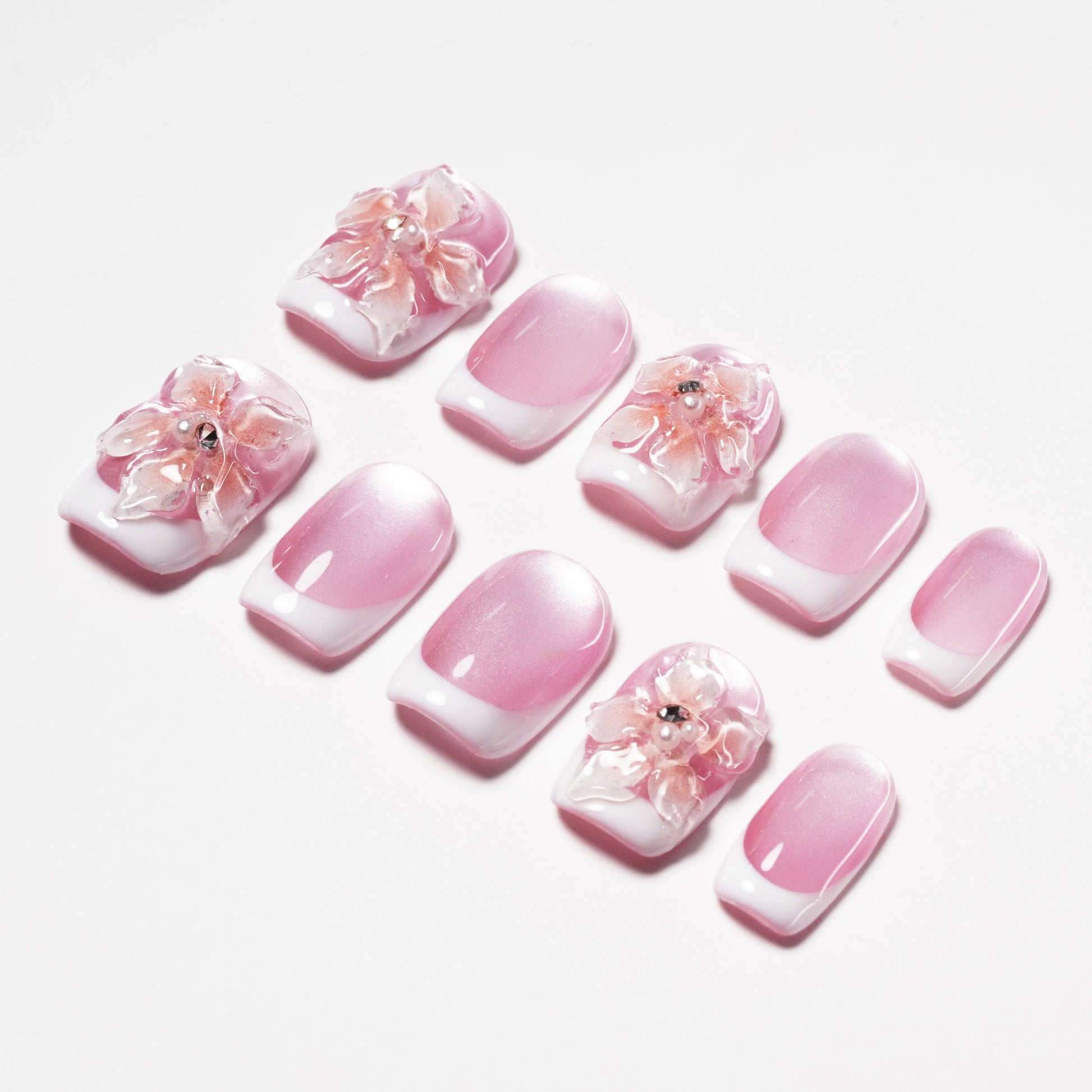 Pink and white press-on nails with 3D floral designs and rhinestone accents on a white background