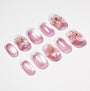Pink press-on nails with white French tips and 3D floral designs, arranged on white background