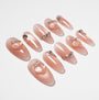 Glossy nude press-on nails with silver rhinestone accents and raised heart designs