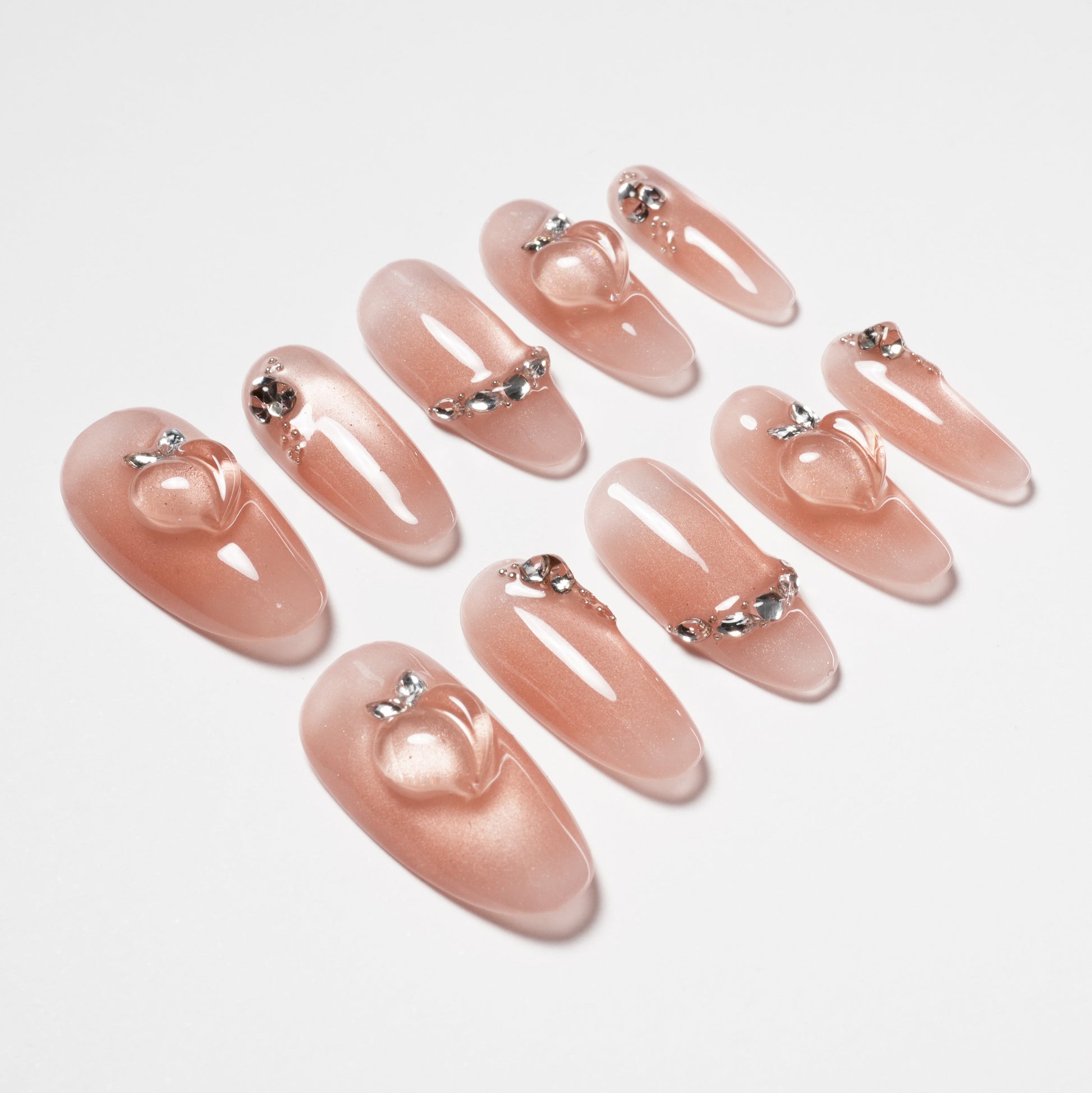 Glossy nude press-on nails with silver rhinestone accents and raised heart designs