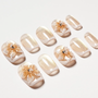 Gold glitter press-on nails with 3D floral accents and rhinestone details, arranged on white background