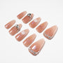 Handmade nude press-on nails with white floral designs, glitter, and gem accents on white background.