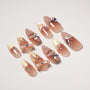 Handmade press-on nails with nude base, gold tips, bows, and pink rhinestone accents