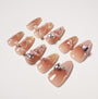 Handmade press-on nails in nude pink with gold glitter tips, bows, pearls, and rhinestone gems.
