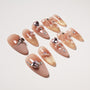 Coffin-shaped nude press-on nails with gold glitter tips, rhinestones, and 3D bows