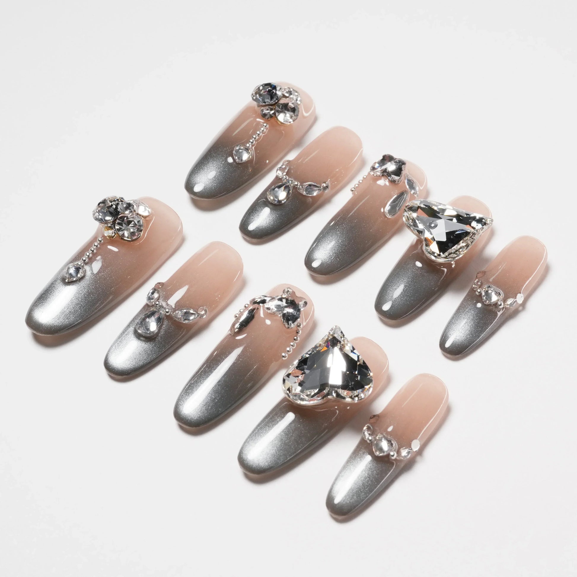 Gray and nude ombre press-on nails with rhinestone and gem embellishments on white background