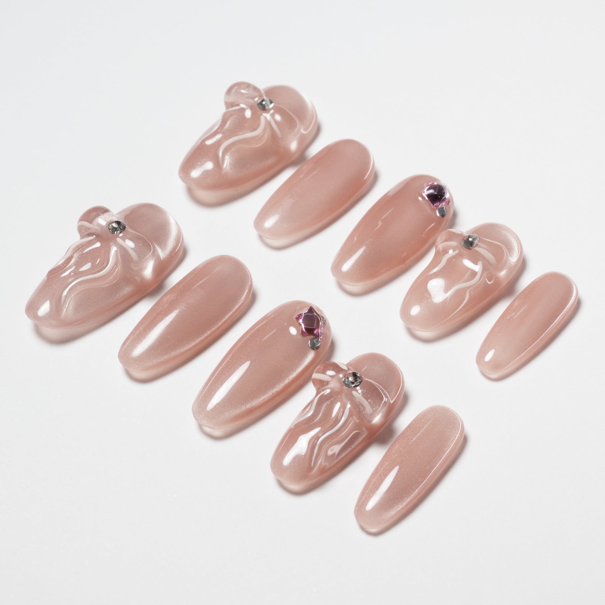 Set of glossy nude pink press-on nails with 3D bow designs and rhinestone accents