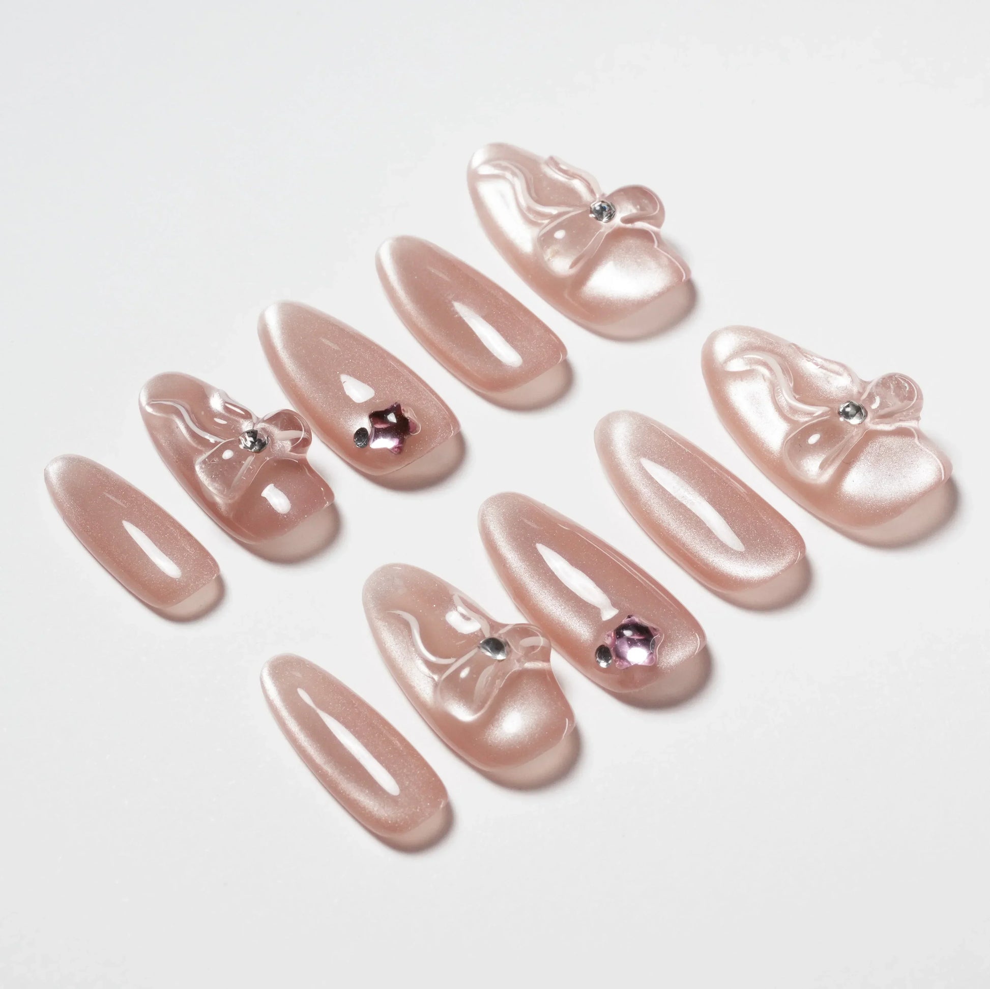 Handmade pink press-on nails with 3D bows and gemstone accents, displayed on white background
