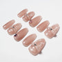 Pink glossy press-on nails with 3D bows and rhinestone accents arranged on white background