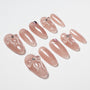 Glossy nude press-on nails with 3D bows and rhinestone accents arranged on white background.
