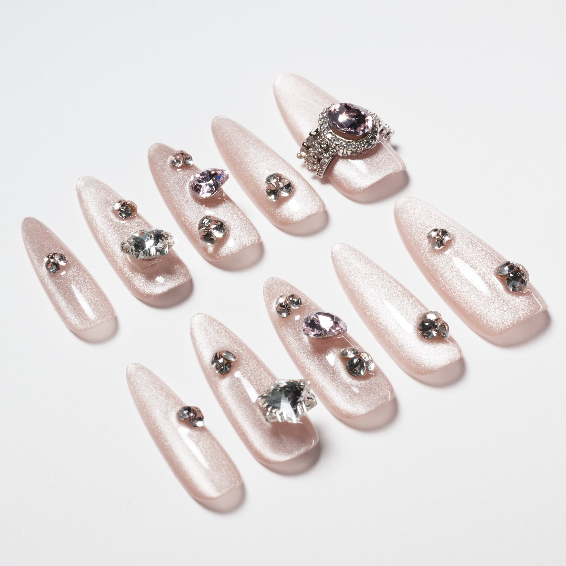 Shimmery pink press-on nails with rhinestone and crystal gem accents, arranged on white background