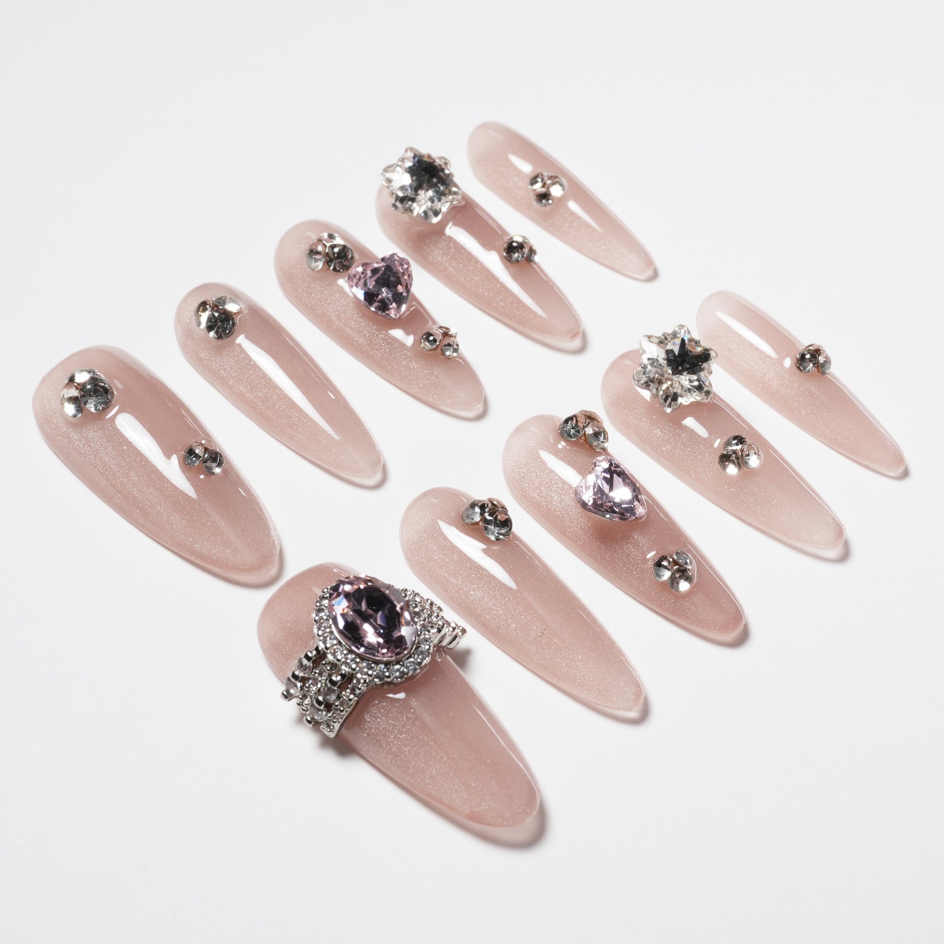 Glossy nude press-on nails decorated with silver rhinestones and large pink gemstone accents