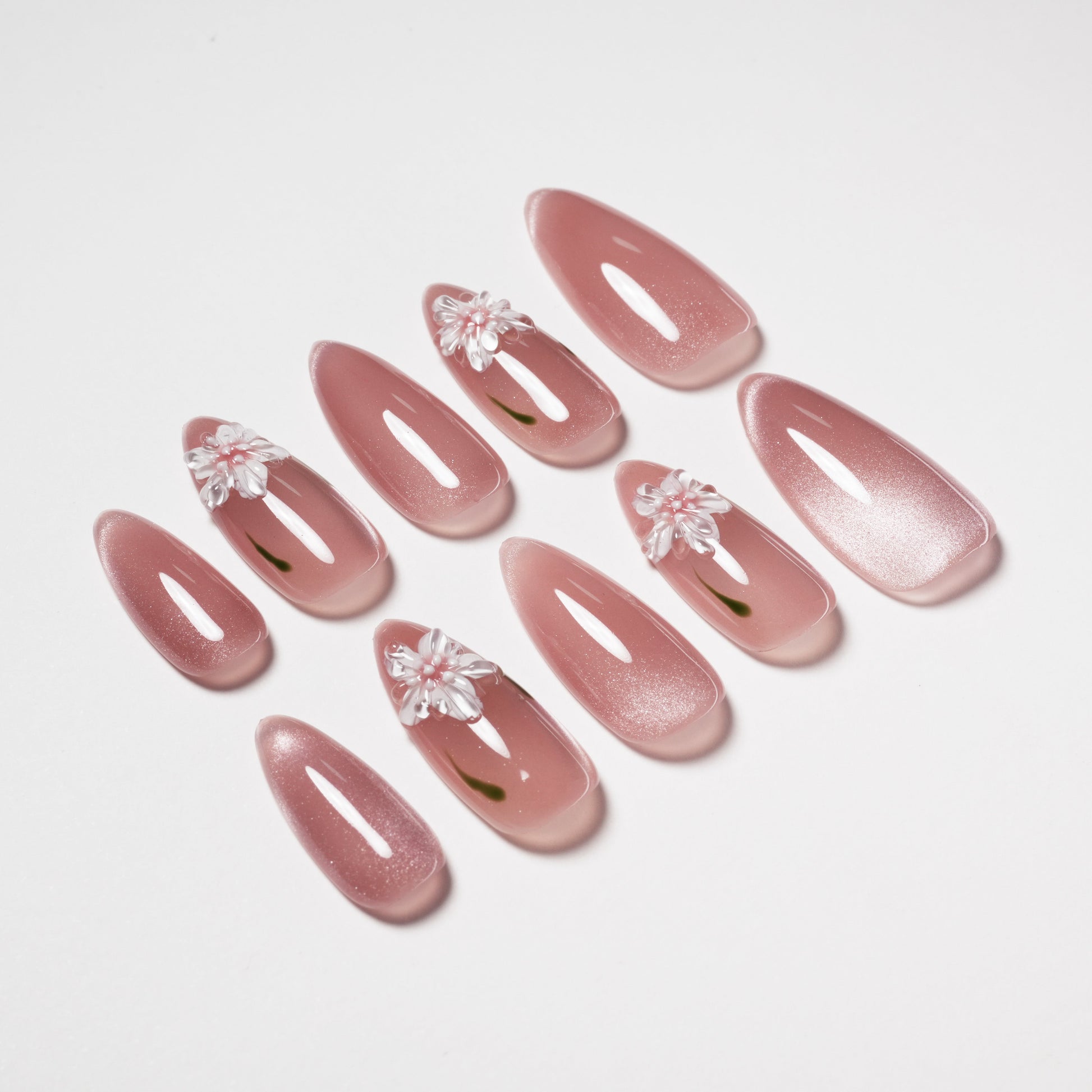 Glossy pink press-on nails with 3D white floral accents, arranged on a white background