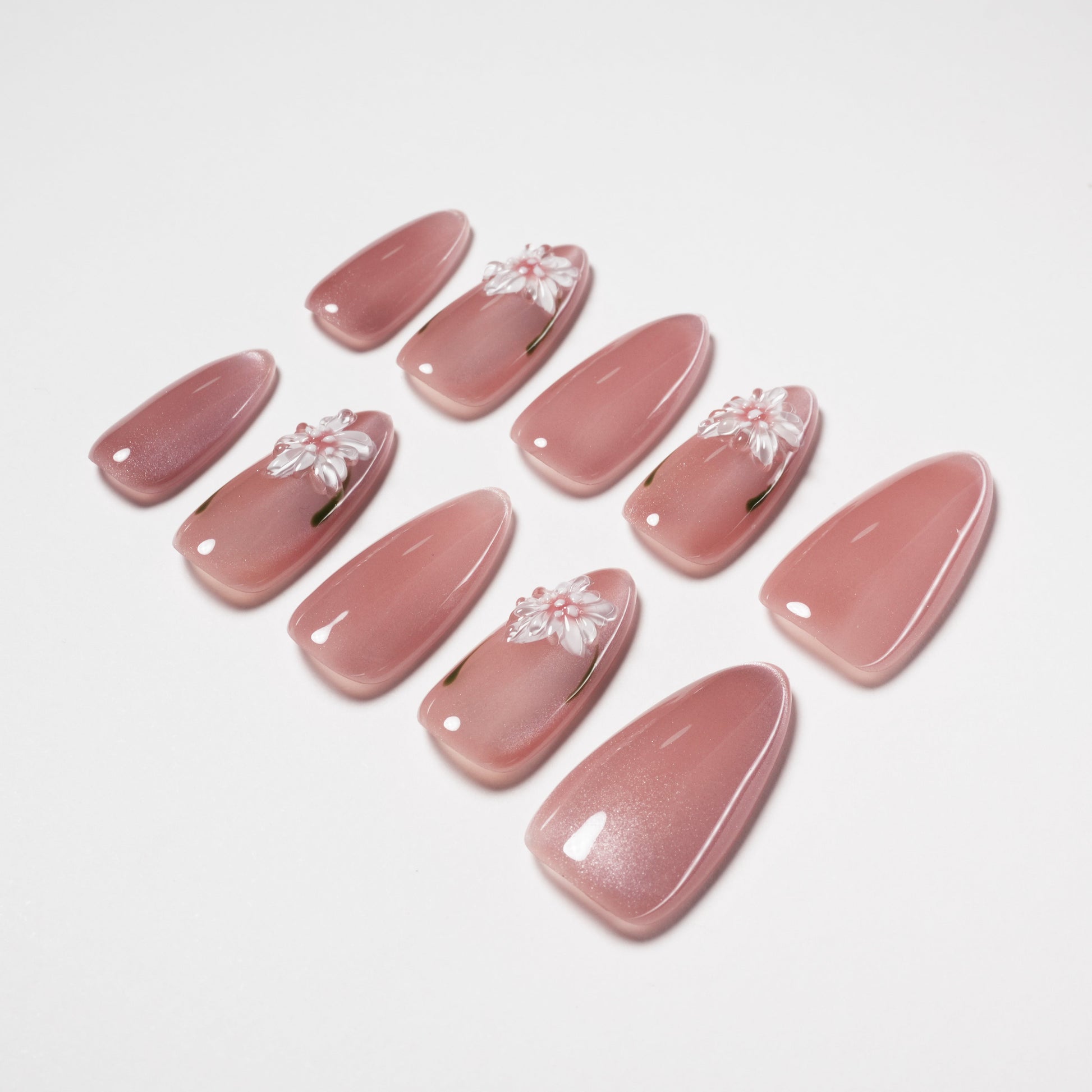 Glossy pink press-on nails with white 3D floral accents, arranged on a white background.