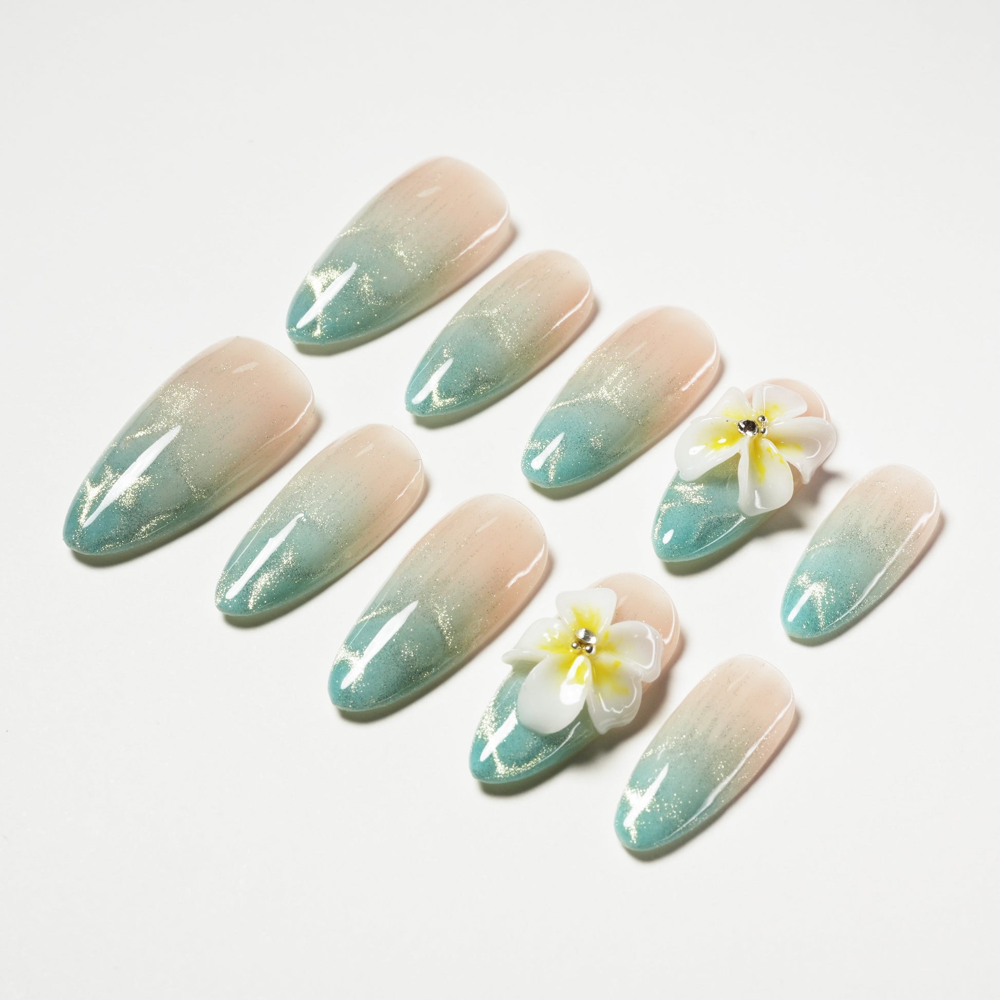 Ombre press-on nails with glitter, blue tips, and 3D floral accents on a white background