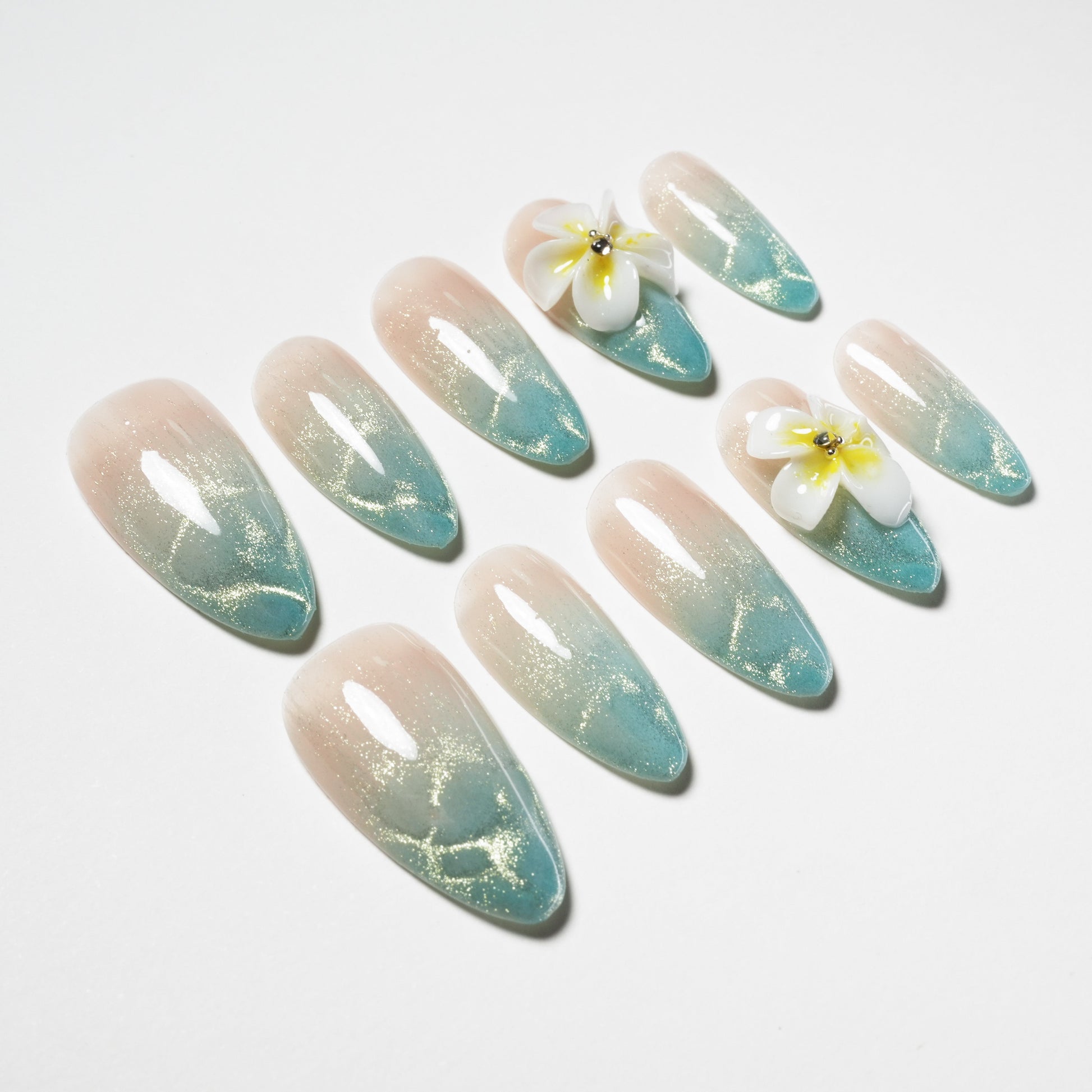 Almond-shaped press-on nails with blue-green ombre, gold shimmer, and 3D floral accents