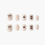 Pink nude press-on nails with black bow and heart designs, glitter accents, on white background.