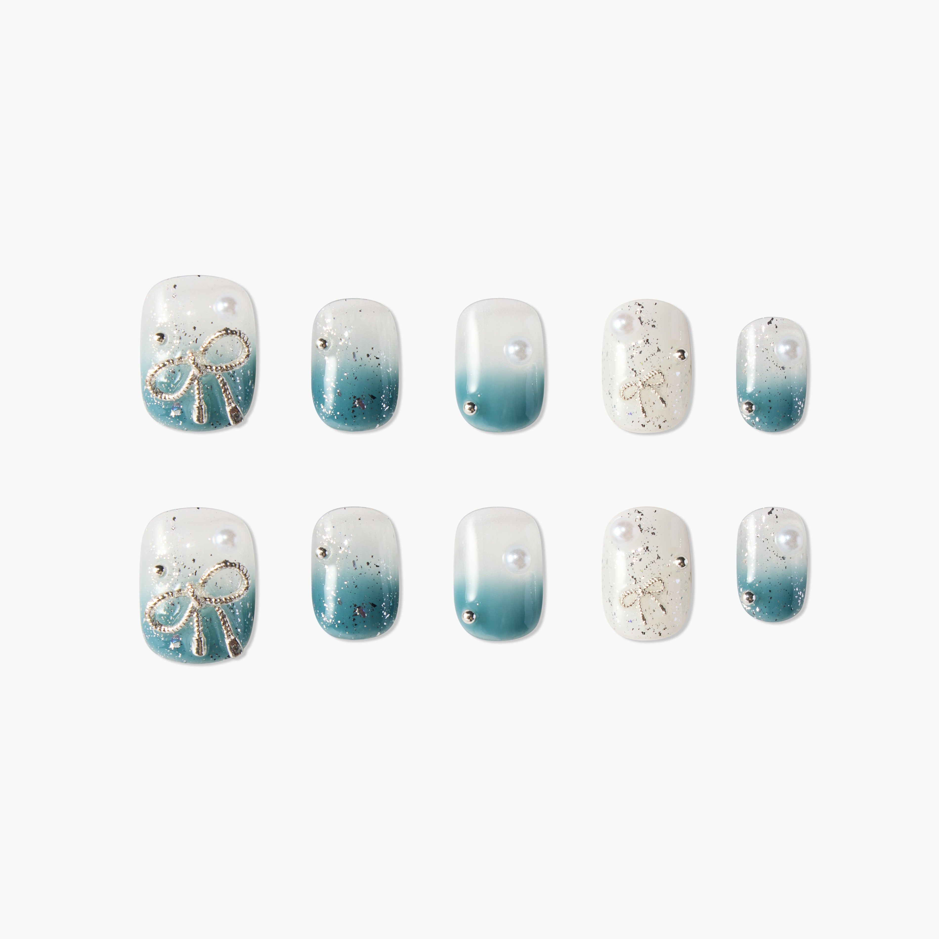 Blue ombre press-on nails with gold bow accents, pearls, and glitter details, arranged on white background.
