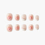 Handmade press-on nails with pink floral design and gold accents on a soft nude base