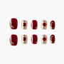 Handmade press-on nails set with glossy burgundy and gold designs, jewel accents, and almond shape