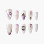 Handmade press-on nails with purple, white, and gold celestial designs and gemstone accents