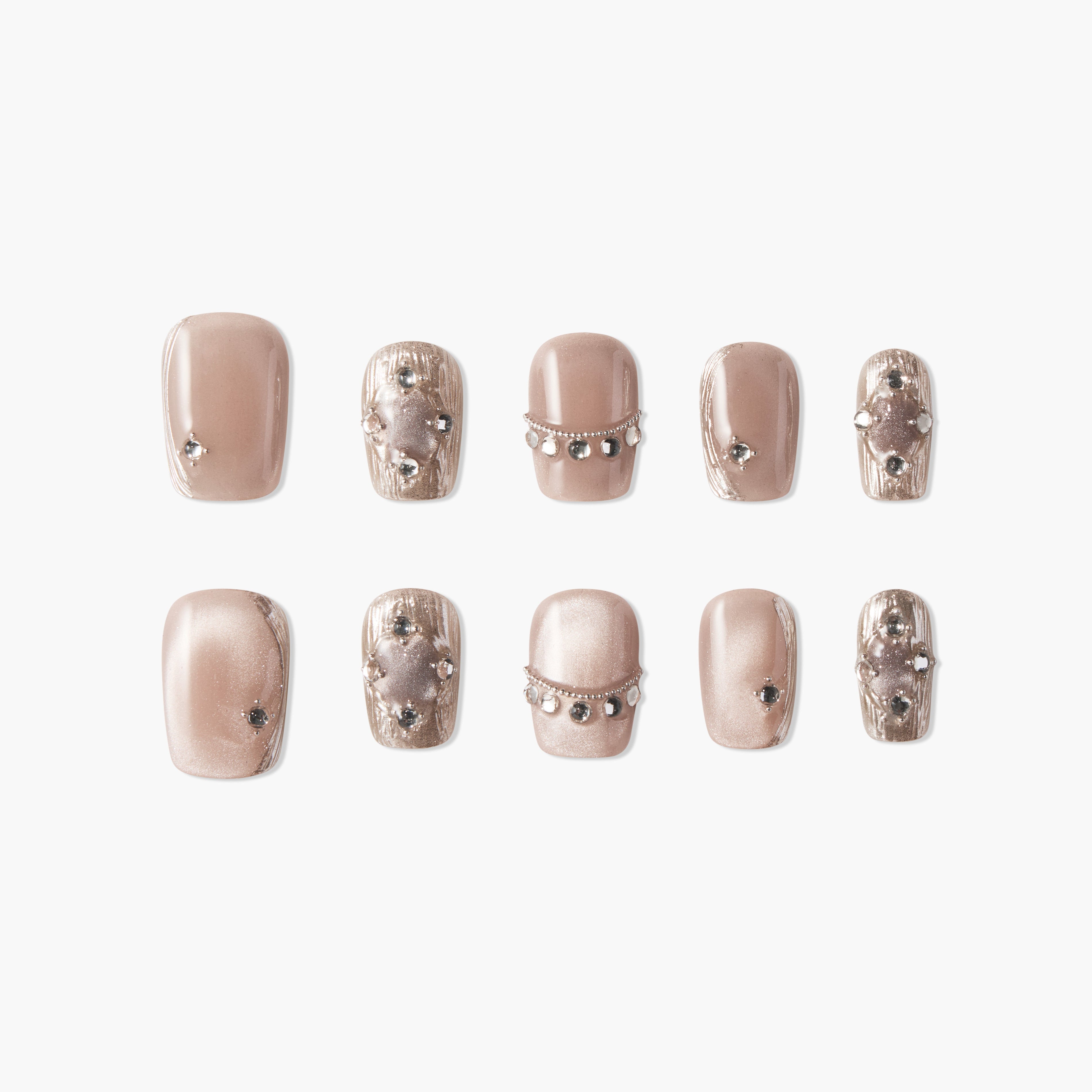 Shimmery nude press-on nails with metallic accents and gem embellishments, arranged in a set.