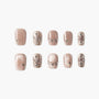 Shimmery nude press-on nails with metallic accents and gem embellishments, arranged in a set.