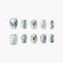 Blue shimmery press-on nails with pearl, gemstone, and glitter accents, mermaid-inspired design.